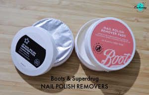 Two round tubs of nail polish remover pads sitting on a wooden surface. On the left is a Superdrug brand tub with a black and white label, shown with its lid off to reveal a silver foil seal. On the right is a Boots brand tub with a coral pink label. Text at the bottom of the image reads "Boots & Superdrug NAIL POLISH REMOVERS."