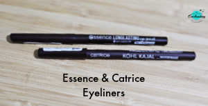 Two black eyeliner pencils lying horizontally on a light-colored wooden surface. The top pencil is the Essence Long Lasting eye pencil, and the bottom one is the Catrice Kohl Kajal Waterproof pencil. Text at the bottom of the image reads "Essence & Catrice Eyeliners."