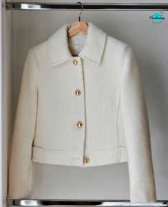 A cream-colored, wool-blended boucle jacket from John Lewis hanging on a wooden hanger inside a closet. The jacket features a structured collar, long sleeves, and four prominent gold buttons down the front.