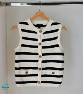 A sleeveless, ivory and navy blue striped knit vest from New Look hanging on a wooden hanger. The vest features a crew neckline, textured knit fabric, and a front button-down closure with gold-toned buttons. It also includes two small faux pockets at the waist, each accented with a matching gold button.