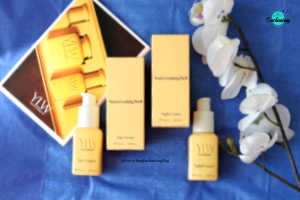Minimalist YLW (You're Looking Well) skincare set featuring buttery-yellow rectangular bottles and matching boxes of Day Cream and Night Cream, with embossed branding and cream-colored pumps, styled next to white orchids on a vibrant deep blue background.