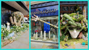 A horizontal collage of three separate vertical photographs displaying different outdoor and storefront floral installations in Chelsea, London.

First panel (far left): A display along a building's exterior featuring a large, sculpted stone hand cradling a patterned sphere, surrounded by a lush bed of white roses, green foliage, and white star decorations.

Second panel (middle): A boutique storefront window under a blue sign that reads "CASSANDRA GOAD." The display features a long, rustic wooden branch extending diagonally across the glass, adorned with miniature climbing figures, over a series of small, vertical stone pillars.

Third panel (far right): A large, stylized head sculpture positioned outdoors. The face features prominent, green textured sunglasses, while the hair is crafted from a dense arrangement of green moss, thick ropes, and small decorative figurines, creating a avant-garde, natural look.
