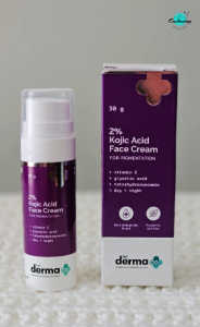 A pump bottle and box of The Derma Co 2% Kojic Acid Face Cream for Pigmentation sitting side-by-side on a textured white surface, with the Everything Enchanting logo in the top-right corner.
