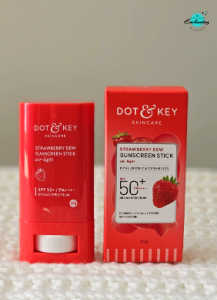 A bright red Dot & Key Skincare Strawberry Dew Sunscreen Stick with SPF 50+ standing next to its matching red product box on a white textured surface, with the Everything Enchanting logo in the top-right corner.