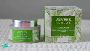 A glass jar of Jovees Herbal Avocado Revitalizing Night Cream with a silver lid sitting next to its green and white leafy packaging box on a white textured surface, with the Everything Enchanting logo in the bottom-left corner.