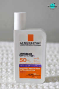 A white bottle of La Roche-Posay Anthelios UVMune 400 Invisible Fluid SPF 50+ sunscreen with orange accents, standing vertically on a white textured surface with the Everything Enchanting logo in the top-right corner.