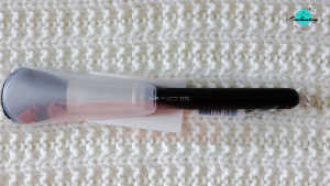 A MAC 129S black makeup brush encased in a protective clear plastic sleeve, laying horizontally on a white textured knitted surface with the Everything Enchanting logo in the top-right corner.