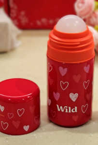 An open refillable Wild roll-on deodorant featuring a red case patterned with pink and white hearts, showing the roller ball top alongside its detached matching red cap.